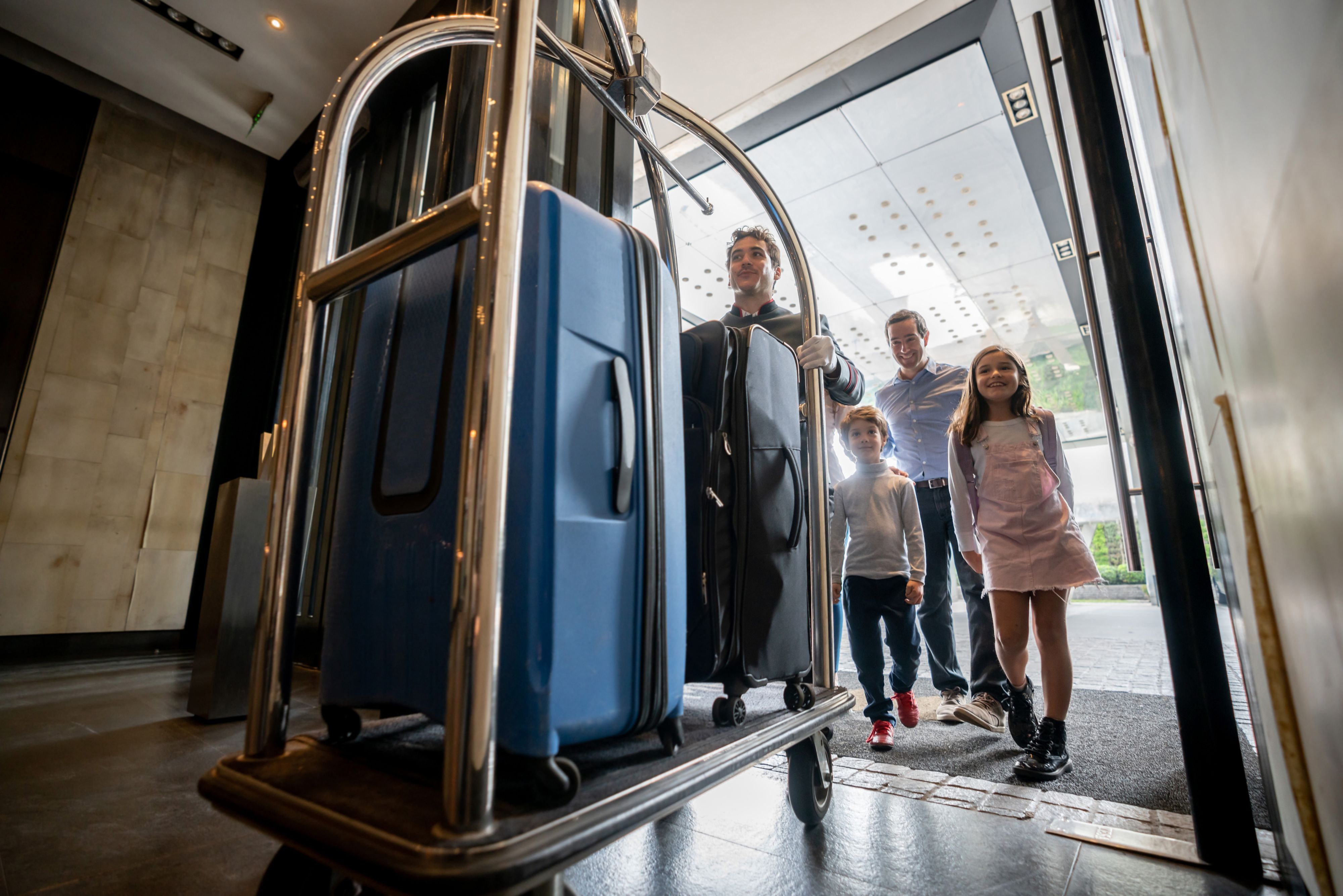 Friendly bellhop pushing cart with guest family luggage on cart ready to check in into hotel - Hotel concepts